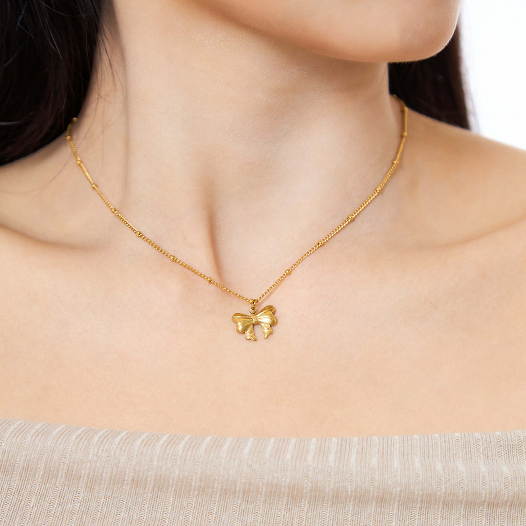 Gold necklace with a bow pendant worn by a person
